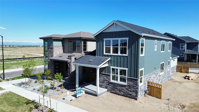 view of front of house with fence, board and batten siding, stone siding, and roof with shingles