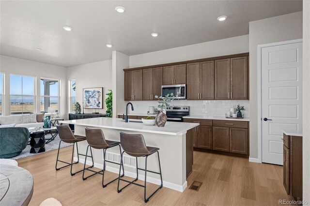 20871 E 60th Ave, Aurora, CO 80019 - kitchen with appliances with stainless steel finishes, open floor plan, light wood-type flooring, a breakfast bar, and an island with sink