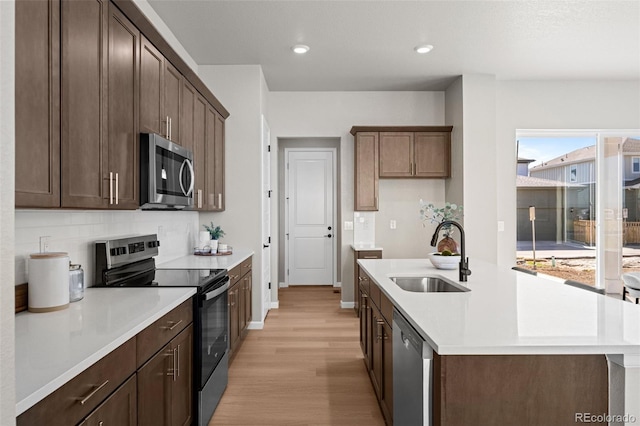 20871 E 60th Ave, Aurora, CO 80019 - kitchen with appliances with stainless steel finishes, a sink, light wood finished floors, light countertops, and a center island with sink