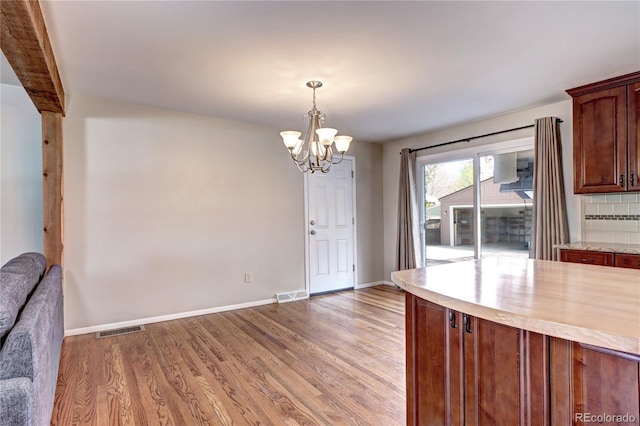 unfurnished dining area with an inviting chandelier, light wood-style flooring, baseboards, and visible vents