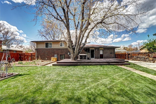 back of property with a lawn, a wooden deck, brick siding, and a fenced backyard