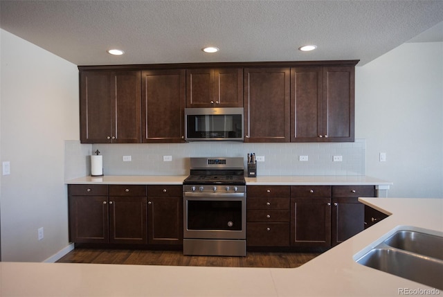 kitchen with backsplash, dark wood-style floors, stainless steel appliances, light countertops, and dark brown cabinets