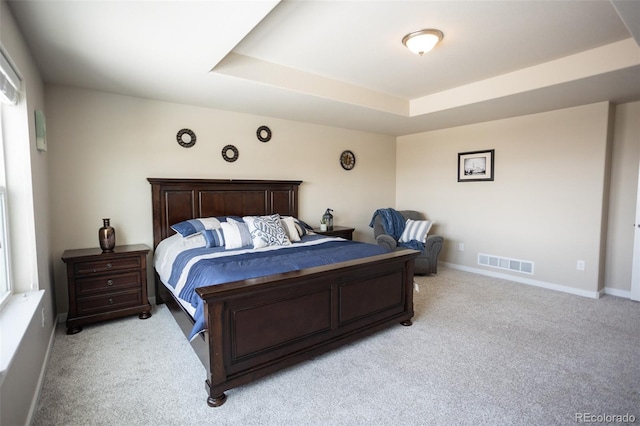 bedroom with a raised ceiling, baseboards, visible vents, and light carpet