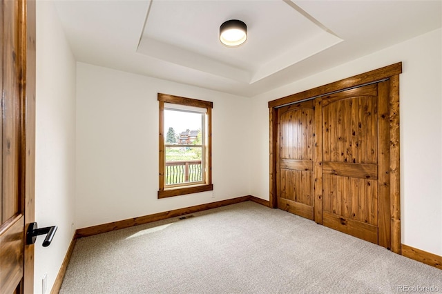 unfurnished bedroom with carpet floors, baseboards, a tray ceiling, and a closet