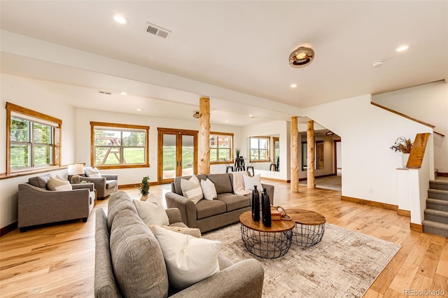 living room featuring stairway, baseboards, light wood-type flooring, decorative columns, and healthy amount of natural light