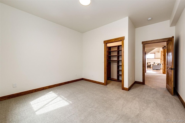 unfurnished bedroom with light carpet, baseboards, and a walk in closet
