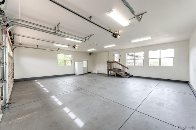 garage with a garage door opener, freestanding refrigerator, and baseboards