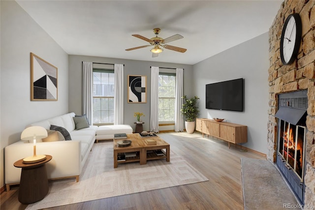 living room with a stone fireplace, ceiling fan, and light hardwood / wood-style floors