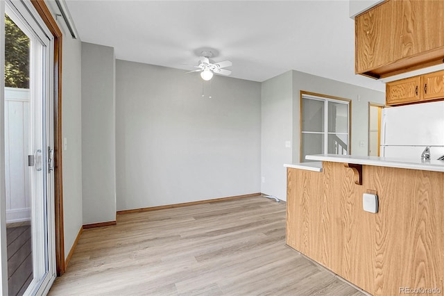 kitchen featuring white refrigerator, ceiling fan, light hardwood / wood-style floors, a kitchen bar, and kitchen peninsula