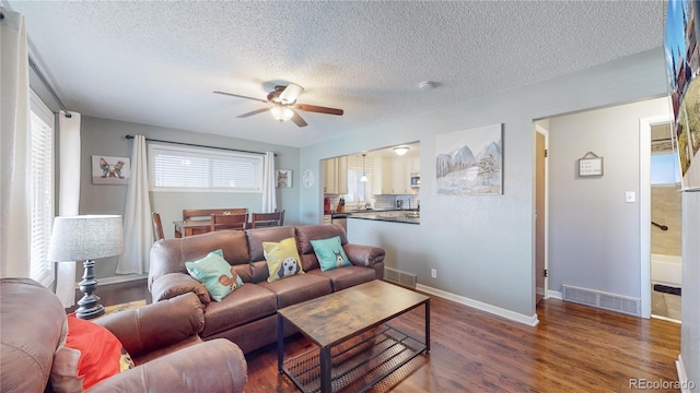 living room with a ceiling fan, wood finished floors, visible vents, and a textured ceiling