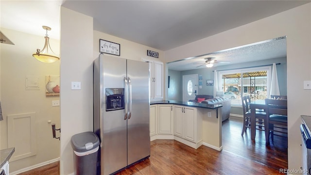 kitchen with dark wood finished floors, a peninsula, ceiling fan, dark countertops, and stainless steel fridge