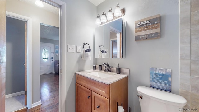 bathroom featuring baseboards, a textured ceiling, vanity, and toilet