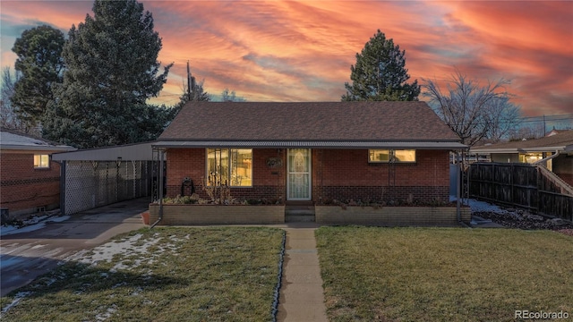 view of front of home with brick siding, a lawn, roof with shingles, and fence
