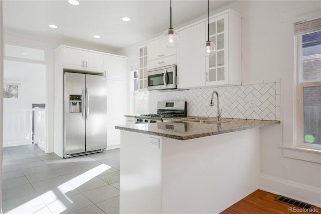 kitchen with appliances with stainless steel finishes, decorative light fixtures, kitchen peninsula, and white cabinets