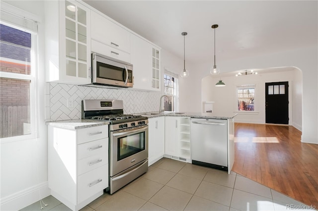 kitchen featuring white cabinetry, stainless steel appliances, tasteful backsplash, light stone countertops, and decorative light fixtures