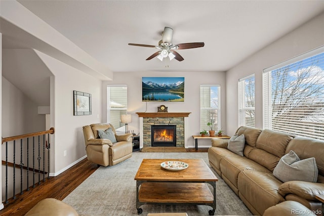 living room with dark wood-type flooring, ceiling fan, and a stone fireplace