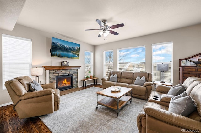 living room featuring hardwood / wood-style flooring, ceiling fan, and a stone fireplace