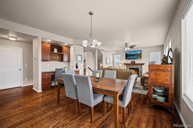 dining area with a fireplace, a healthy amount of sunlight, dark hardwood / wood-style flooring, and ceiling fan with notable chandelier