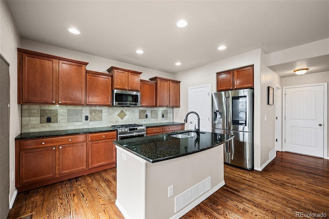 kitchen featuring sink, dark stone countertops, stainless steel appliances, an island with sink, and dark hardwood / wood-style flooring