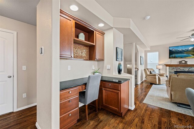 kitchen featuring ceiling fan, dark hardwood / wood-style floors, built in desk, and a fireplace