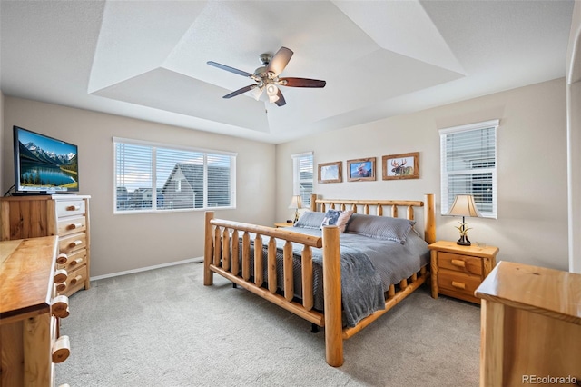 carpeted bedroom with a raised ceiling and ceiling fan