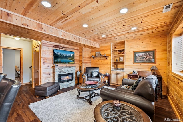 living room with dark wood-type flooring, wood walls, a stone fireplace, and wooden ceiling