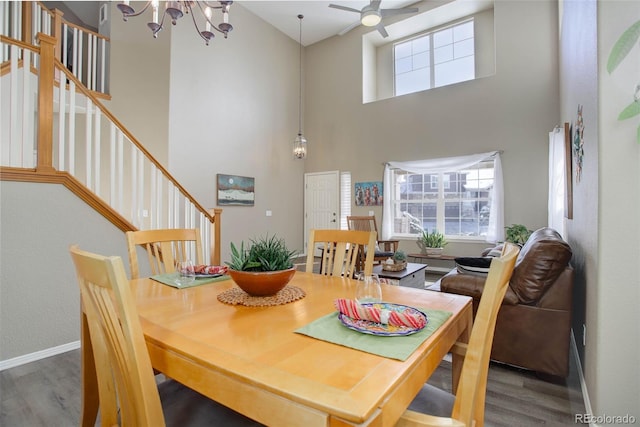 dining space featuring wood-type flooring, ceiling fan with notable chandelier, and a high ceiling