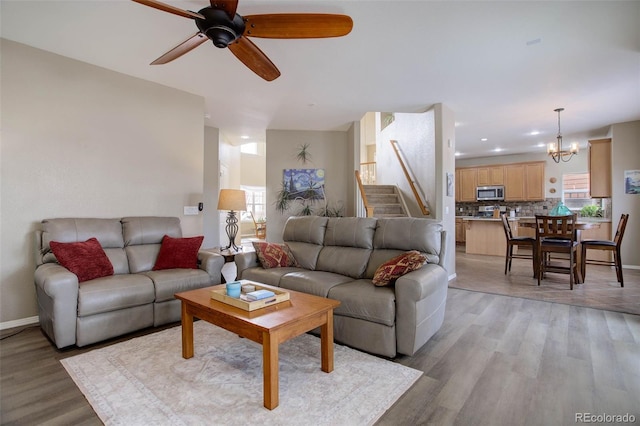 living room with ceiling fan with notable chandelier and light hardwood / wood-style flooring