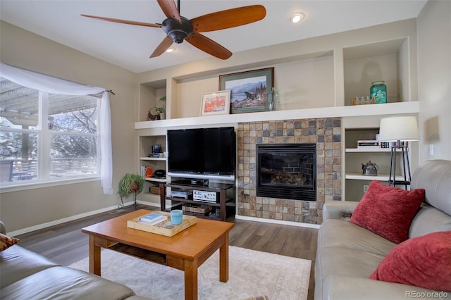 living room featuring hardwood / wood-style flooring, ceiling fan, built in shelves, and a tiled fireplace