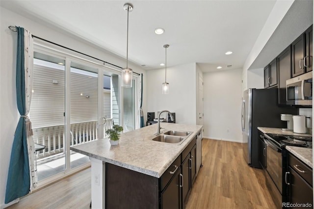 kitchen featuring appliances with stainless steel finishes, a sink, light countertops, light wood-style floors, and an island with sink