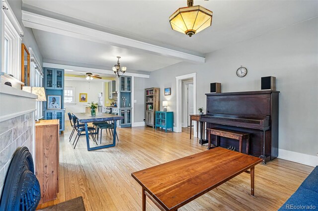 living room featuring a ceiling fan, a tiled fireplace, baseboards, beamed ceiling, and light wood-style floors