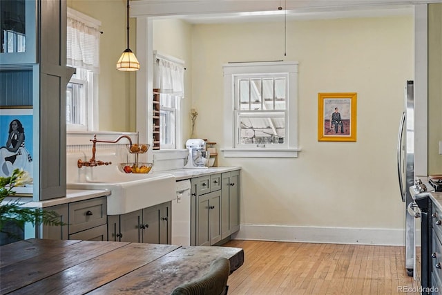 kitchen with a sink, light wood-type flooring, baseboards, decorative light fixtures, and gray cabinetry
