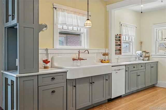 bar with decorative light fixtures, light wood-type flooring, a sink, and white dishwasher