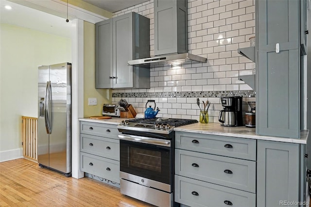 kitchen featuring wall chimney exhaust hood, appliances with stainless steel finishes, gray cabinetry, and tasteful backsplash