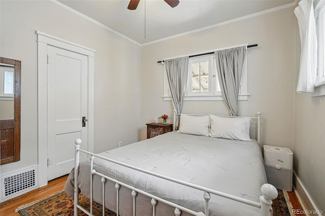 bedroom with ceiling fan, crown molding, visible vents, and wood finished floors