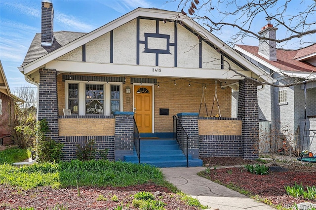 bungalow-style house featuring a chimney, a porch, stucco siding, and brick siding