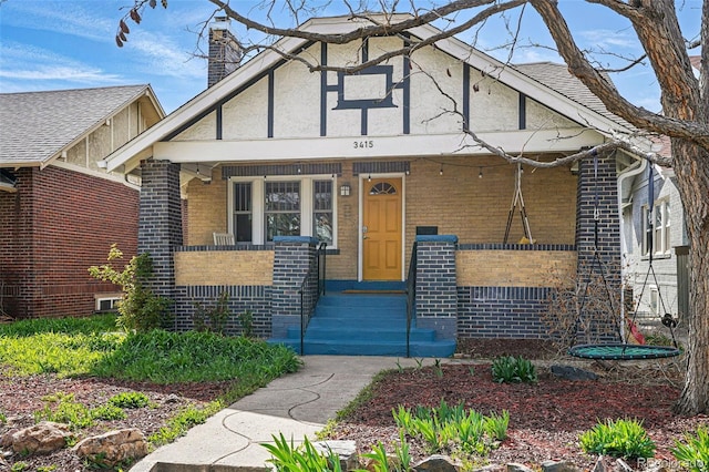 view of front of property with a chimney, stucco siding, brick siding, and covered porch