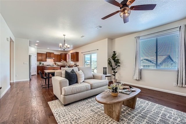 living room with ceiling fan with notable chandelier and dark hardwood / wood-style flooring