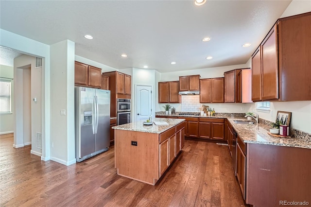 kitchen featuring appliances with stainless steel finishes, dark hardwood / wood-style flooring, a kitchen island, and light stone counters