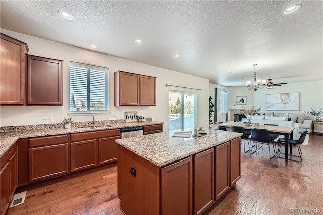 kitchen with sink, dark wood-type flooring, stainless steel dishwasher, a textured ceiling, and decorative light fixtures