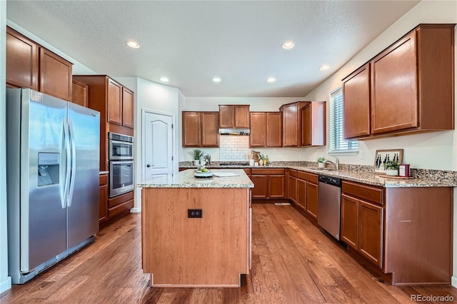 kitchen with light stone countertops, a kitchen island, appliances with stainless steel finishes, and wood finished floors