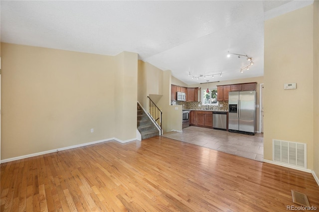 unfurnished living room featuring a notable chandelier, rail lighting, vaulted ceiling, and light hardwood / wood-style flooring