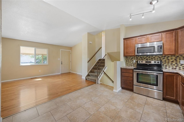 kitchen with light hardwood / wood-style flooring, vaulted ceiling, decorative backsplash, appliances with stainless steel finishes, and a textured ceiling