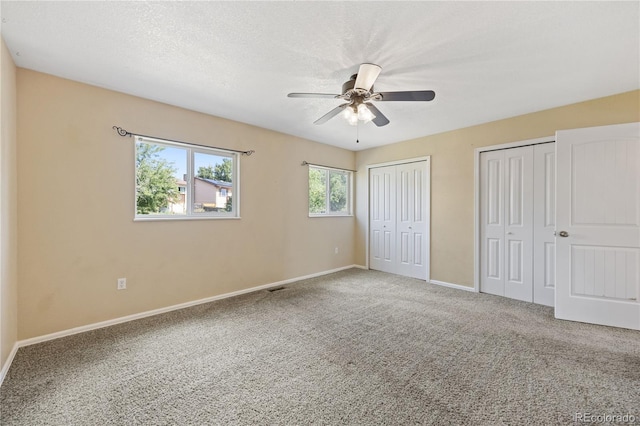 unfurnished bedroom featuring a textured ceiling, ceiling fan, two closets, and carpet flooring