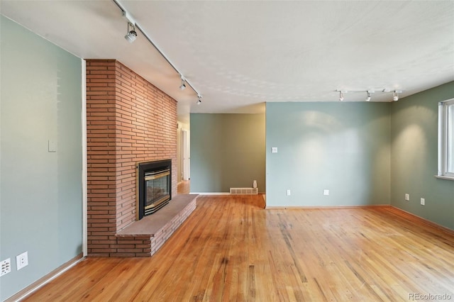 3784 Swadley St, Wheat Ridge, CO 80033 - unfurnished living room with rail lighting, wood-type flooring, and a brick fireplace