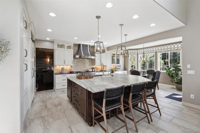 17490 W 67th Ave, Arvada, CO 80007 - kitchen with wall chimney range hood, a large island, backsplash, white cabinetry, and glass insert cabinets
