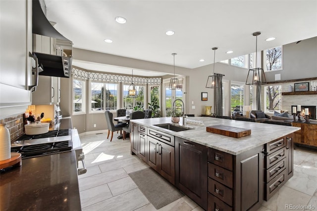 17490 W 67th Ave, Arvada, CO 80007 - kitchen featuring a stone fireplace, a sink, dark brown cabinetry, recessed lighting, and an island with sink