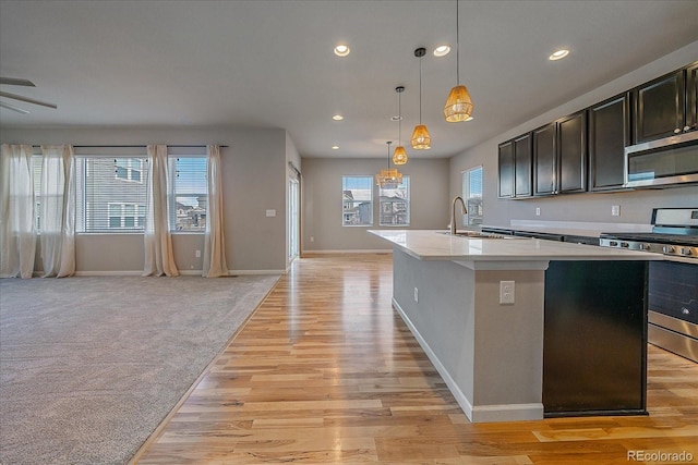 kitchen with light carpet, hanging light fixtures, ceiling fan, an island with sink, and stainless steel appliances