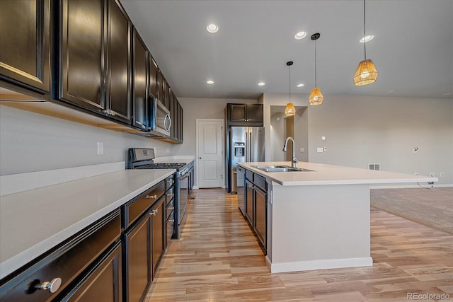 kitchen featuring a kitchen island with sink, hanging light fixtures, sink, light hardwood / wood-style floors, and stainless steel appliances