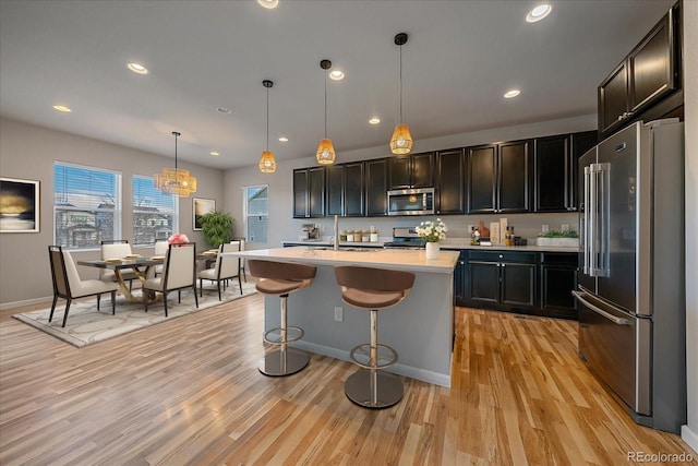 kitchen featuring appliances with stainless steel finishes, a breakfast bar, sink, hanging light fixtures, and a kitchen island with sink